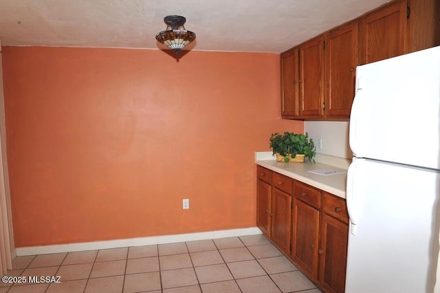 kitchen featuring brown cabinetry, freestanding refrigerator, light countertops, and light tile patterned floors