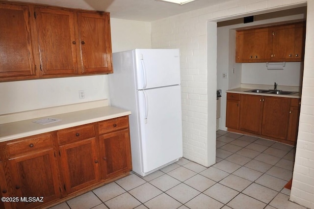 kitchen with brown cabinets, light countertops, a sink, and freestanding refrigerator