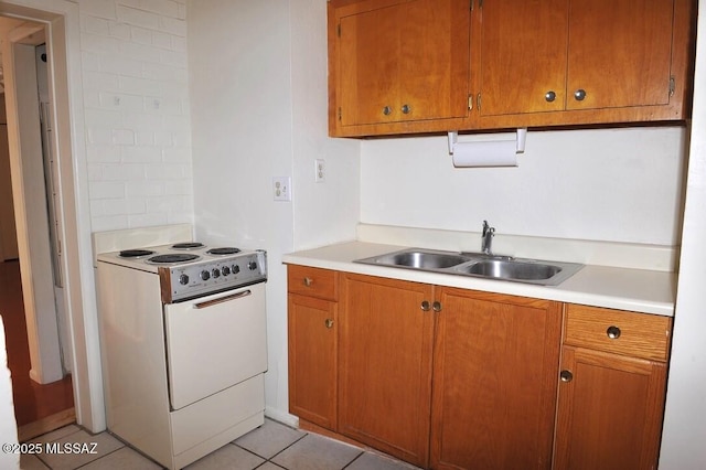 kitchen with light tile patterned floors, a sink, light countertops, brown cabinets, and white electric range oven