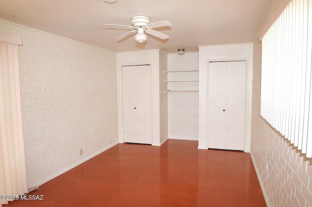 unfurnished bedroom featuring concrete flooring, brick wall, ceiling fan, and multiple closets