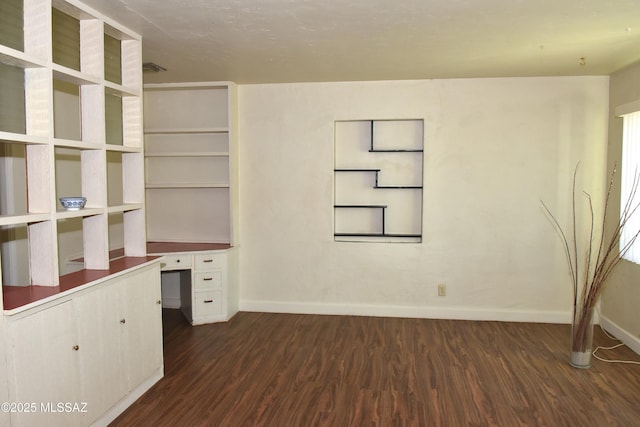 unfurnished office featuring dark wood-style floors, built in study area, and baseboards