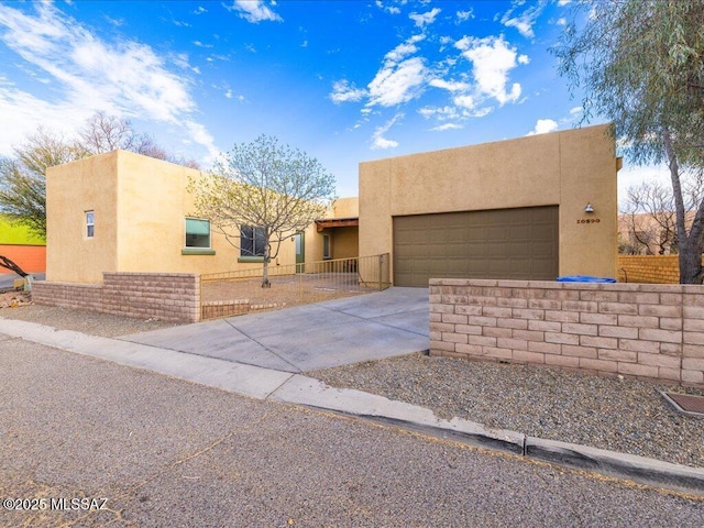 pueblo-style home featuring a garage, driveway, fence, and stucco siding