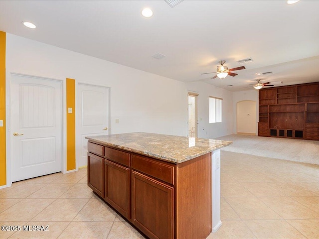 10590 E Maldonado Pl, Tucson, AZ 85747 - kitchen with a ceiling fan, light tile patterned flooring, arched walkways, a kitchen island, and light stone counters