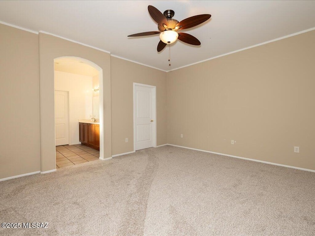 unfurnished bedroom featuring ensuite bathroom, ornamental molding, arched walkways, and light colored carpet