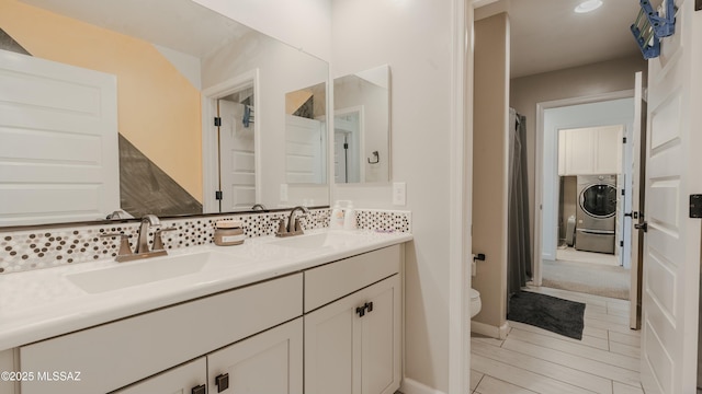 bathroom with toilet, double vanity, a sink, and washer / dryer