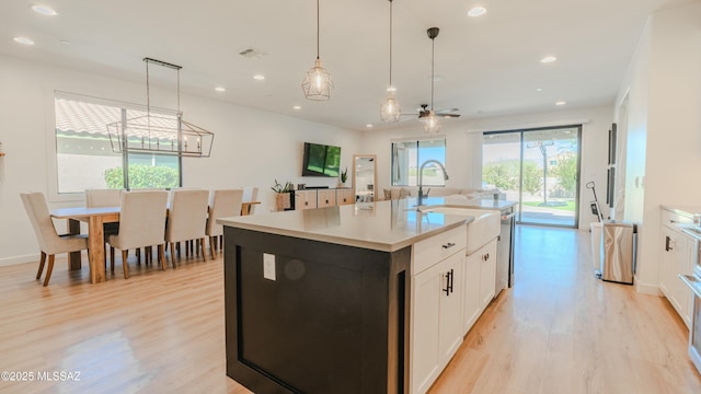 kitchen with recessed lighting, light countertops, light wood-style flooring, white cabinetry, and a kitchen island with sink