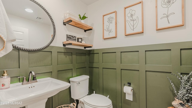 bathroom with toilet, visible vents, a decorative wall, and a sink