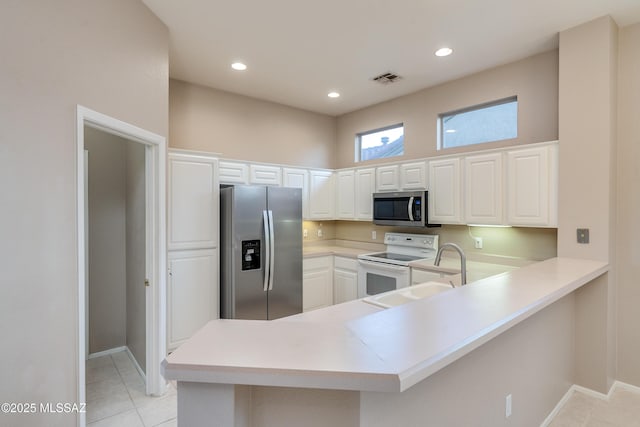 kitchen with a peninsula, stainless steel appliances, light countertops, white cabinetry, and a sink