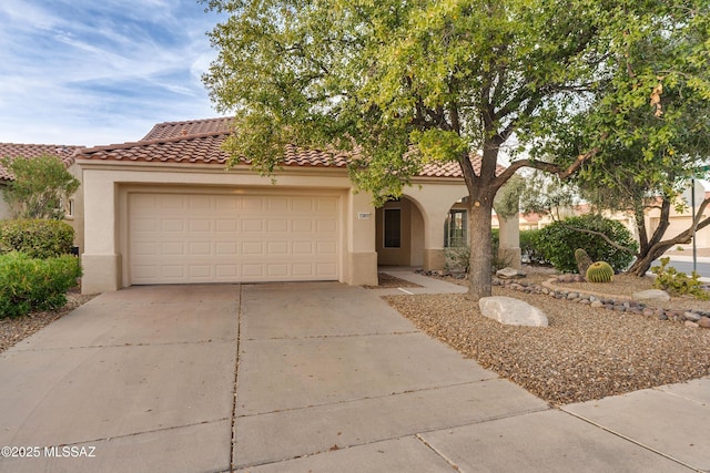 mediterranean / spanish house with an attached garage, a tiled roof, concrete driveway, and stucco siding