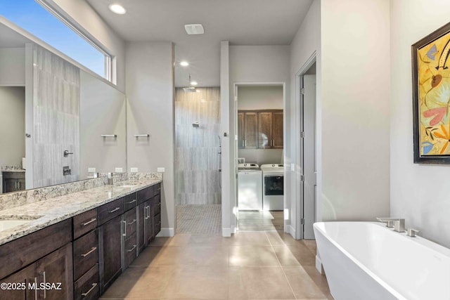 full bath featuring washer and clothes dryer, double vanity, a sink, a tile shower, and a freestanding tub