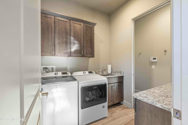 washroom featuring washing machine and dryer, cabinet space, a sink, and light wood finished floors