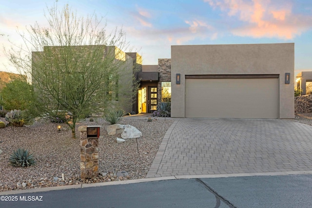 adobe home with an attached garage, stone siding, decorative driveway, and stucco siding