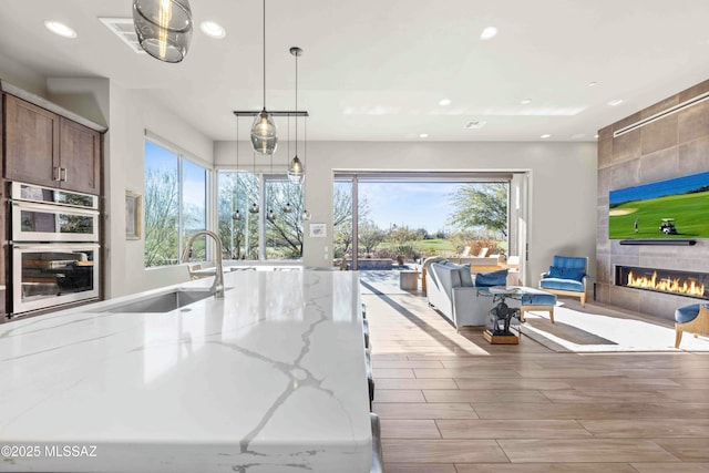 kitchen with light stone countertops, stainless steel double oven, a sink, and recessed lighting