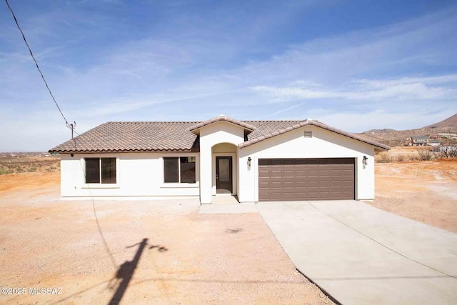 mediterranean / spanish house with a garage, concrete driveway, a tiled roof, and stucco siding