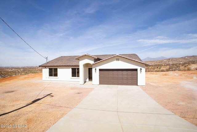 mediterranean / spanish-style home with a garage, driveway, a tiled roof, and stucco siding