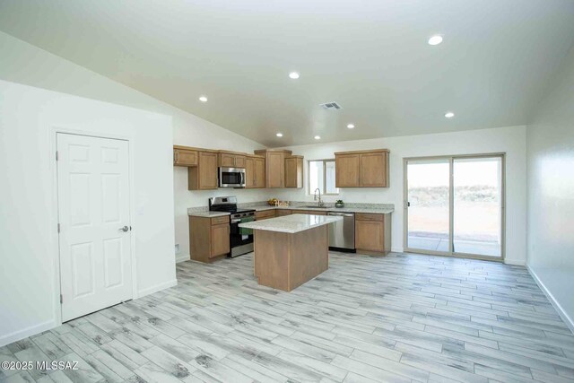 kitchen featuring light countertops, appliances with stainless steel finishes, brown cabinetry, a sink, and a kitchen island