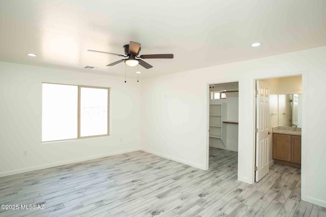 unfurnished bedroom with light wood-type flooring, a walk in closet, visible vents, and baseboards