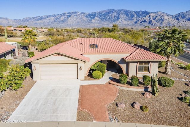 mediterranean / spanish-style house with an attached garage, a mountain view, a tiled roof, concrete driveway, and stucco siding