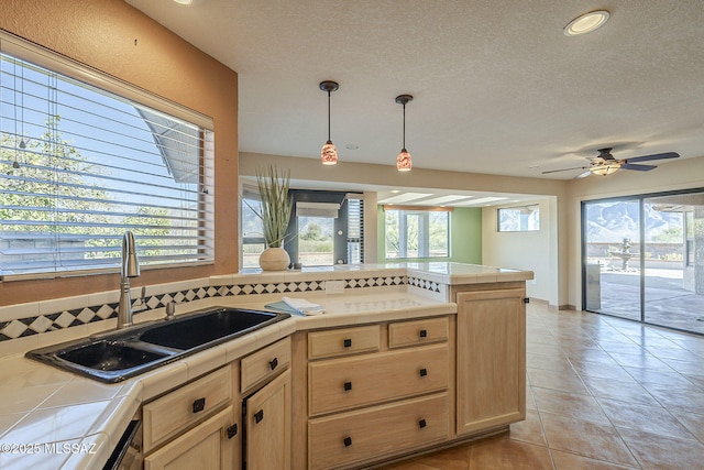 kitchen featuring tile countertops, a peninsula, a sink, and light brown cabinets