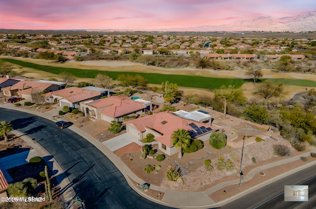 aerial view at dusk featuring view of golf course, a residential view, and a mountain view