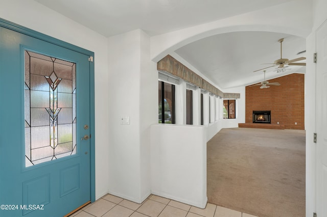 foyer entrance with light tile patterned floors, light colored carpet, lofted ceiling, ceiling fan, and a brick fireplace