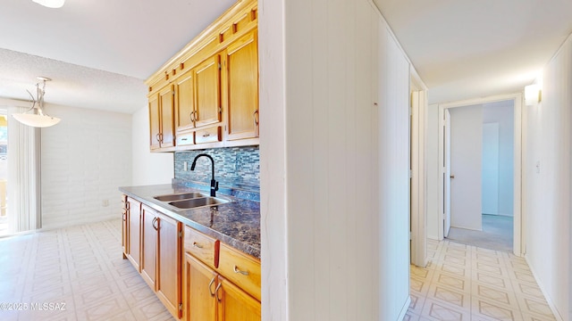 kitchen featuring dark countertops, decorative light fixtures, a sink, light floors, and backsplash