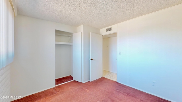 unfurnished bedroom featuring a textured ceiling, carpet floors, a closet, and visible vents