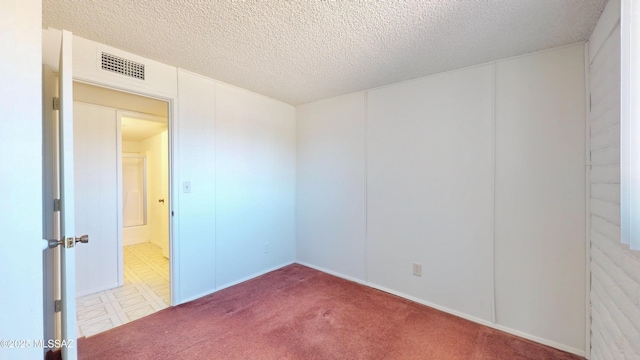 carpeted spare room featuring a textured ceiling and visible vents