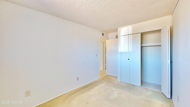 unfurnished bedroom featuring light carpet, a textured ceiling, visible vents, and a closet