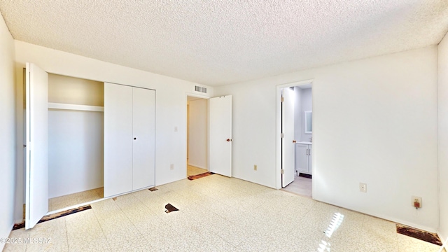 unfurnished bedroom with a closet, visible vents, connected bathroom, a textured ceiling, and tile patterned floors