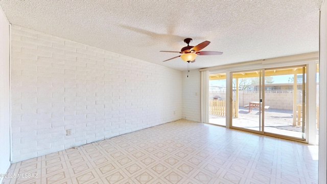 spare room featuring brick wall, a textured ceiling, a ceiling fan, and tile patterned floors