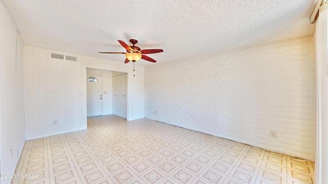 unfurnished room featuring light floors, visible vents, a ceiling fan, a textured ceiling, and brick wall