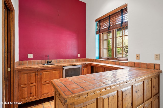 kitchen with wine cooler, a sink, and tile counters