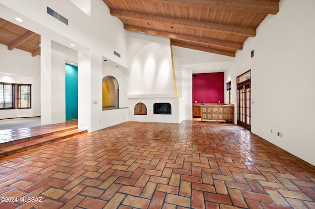 unfurnished living room with a large fireplace, visible vents, wood ceiling, brick floor, and beam ceiling