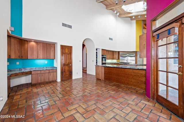 kitchen with arched walkways, beam ceiling, brown cabinets, visible vents, and wall oven