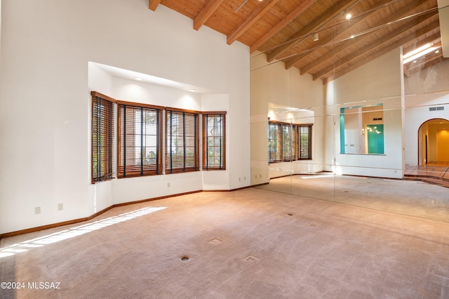 empty room with carpet floors, arched walkways, wood ceiling, beamed ceiling, and baseboards