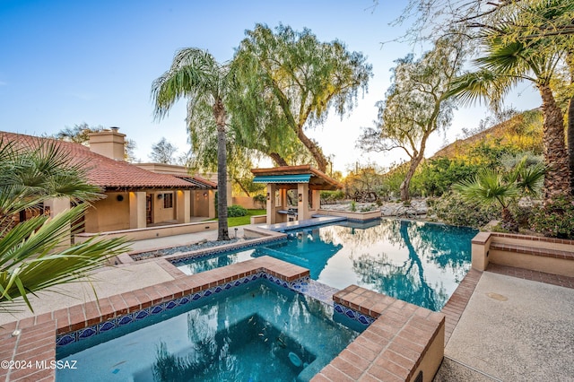 view of pool featuring a pool with connected hot tub, an exterior structure, and a patio