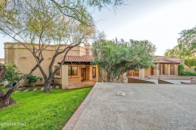 view of front facade featuring a front lawn, a patio area, a tile roof, and stucco siding