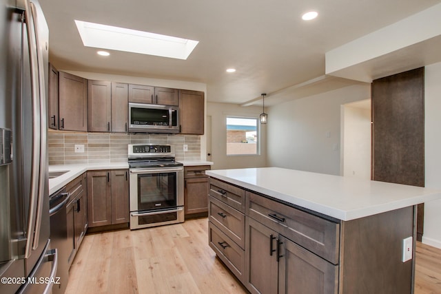 kitchen with a skylight, tasteful backsplash, stainless steel appliances, light countertops, and light wood-style floors