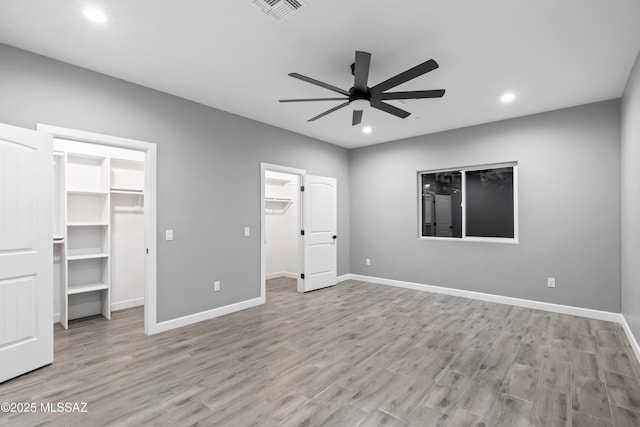 unfurnished bedroom featuring wood finished floors, a walk in closet, visible vents, and baseboards