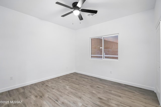 spare room featuring a ceiling fan, visible vents, baseboards, and wood finished floors