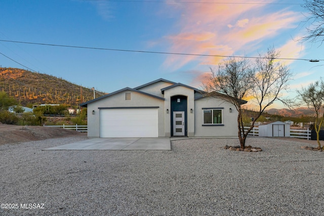 view of front facade with driveway, a garage, fence, a shed, and stucco siding