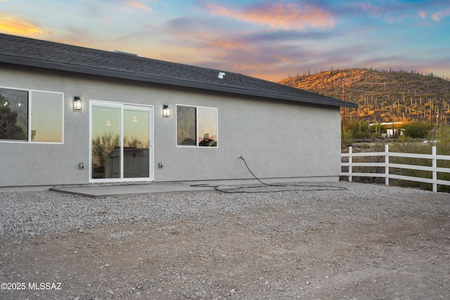 rear view of house with a patio, roof with shingles, fence, and stucco siding