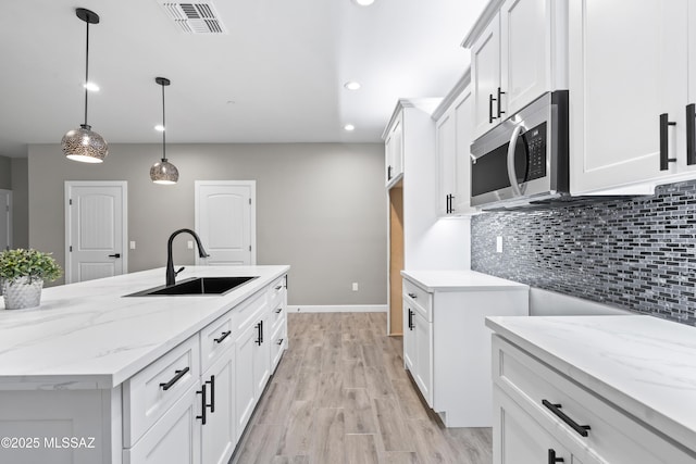 kitchen with light stone counters, a sink, visible vents, backsplash, and stainless steel microwave