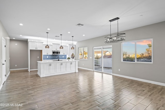 kitchen with visible vents, decorative backsplash, open floor plan, light countertops, and a sink