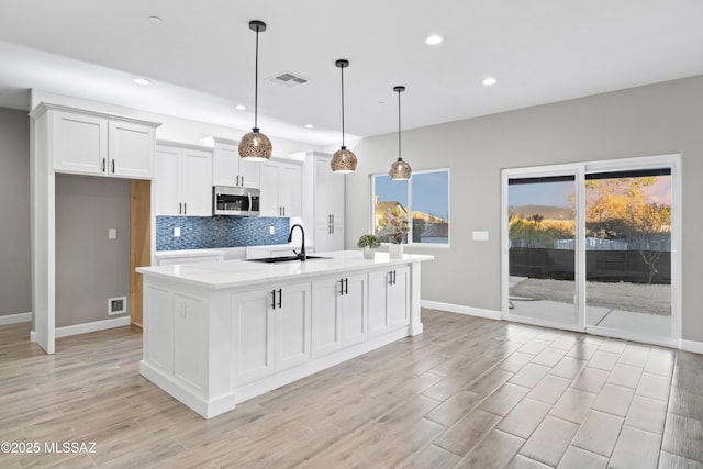 kitchen featuring a sink, visible vents, white cabinets, tasteful backsplash, and stainless steel microwave