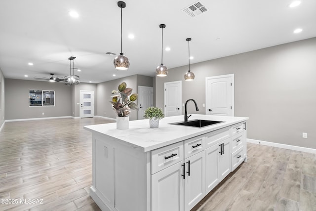 kitchen featuring visible vents, white cabinets, a kitchen island with sink, light wood-style floors, and a sink