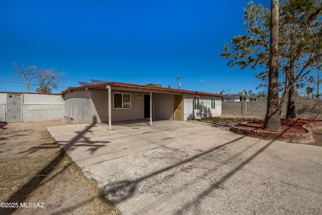 back of property featuring roof mounted solar panels, fence, and stucco siding