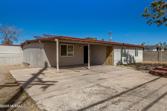 back of house with a patio, solar panels, stucco siding, fence, and driveway