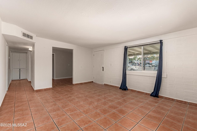 unfurnished room featuring light tile patterned floors, brick wall, and visible vents